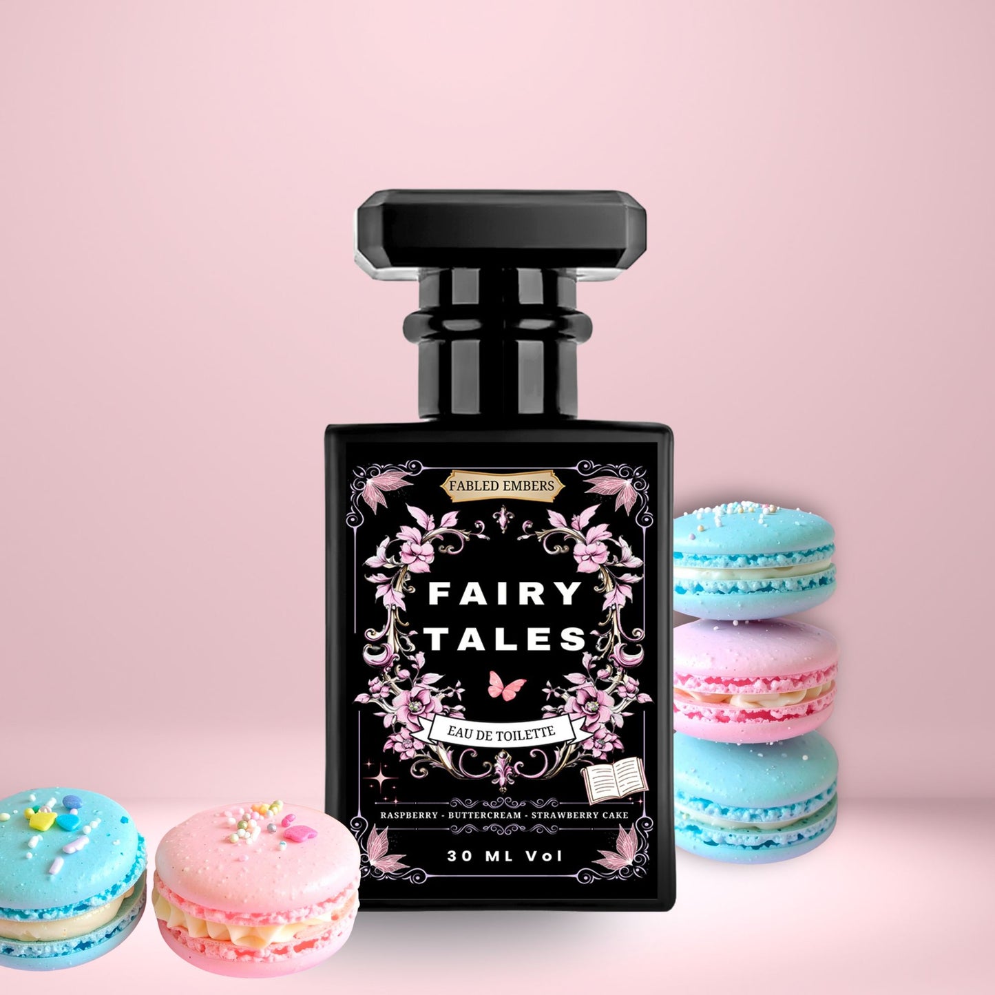 Fairy Tales EDT Perfume in a sleek matte black bottle with a pink floral high contrast label. Smells like Raspberry Strawberry Cake and Buttercream, on a soft pink background with blue and pink macarons.