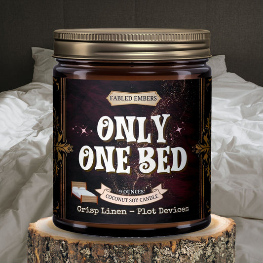 Amber jar "Only One Bed" candle. The playful label showcases a bed icon and witty text about "Plot Devices." Scent notes: Crisp Linen. Perfect for bookworms who love a good romance trope.