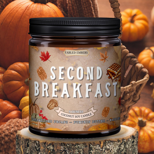 Candle jar labeled 'Second Breakfast' surrounded by pumpkins on a wooden surface