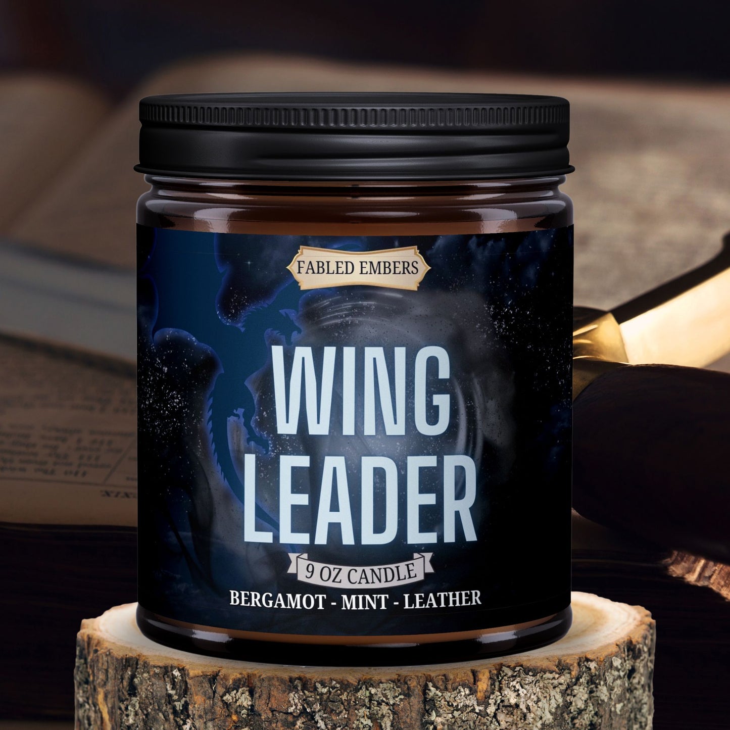 Wing Leader candle by Fabled Embers featuring a blue dragon on a label with shadow moitiffs, amber glass jar sitting on a wood riser, with a sword and book in the background