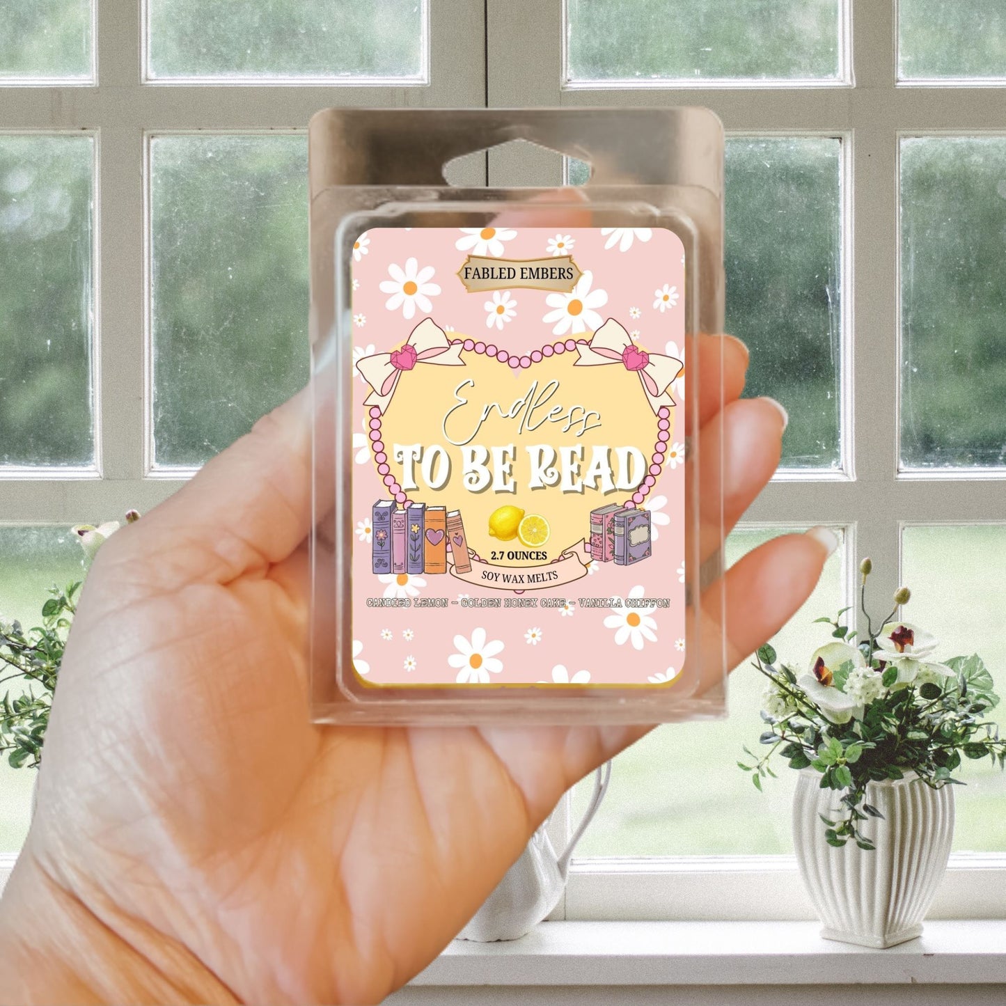 Hand holding a wax melt package with a window and plants in the background