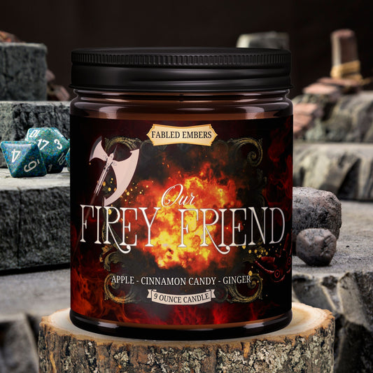 A jar candle with a label featuring a illustration of a character and text that reads 'OUR FIERY FRIEND apples + ginger + cinnamon' in a stoney background with dice.