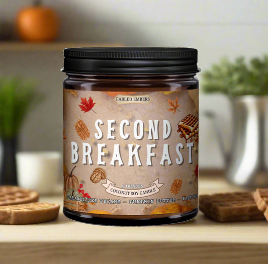Candle jar labeled 'Second Breakfast' with autumn-themed design on a wooden surface.