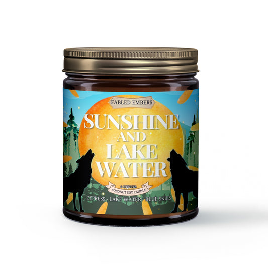 "Sunshine and Lake Water" coconut soy candle. Its vibrant label features howling wolves silhouetted against a setting sun, with a whimsical forest and bright blue skies. 
