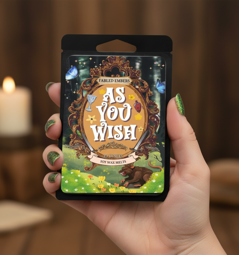 Hand holding a 'As You Wish' product packaging with a candle in the background