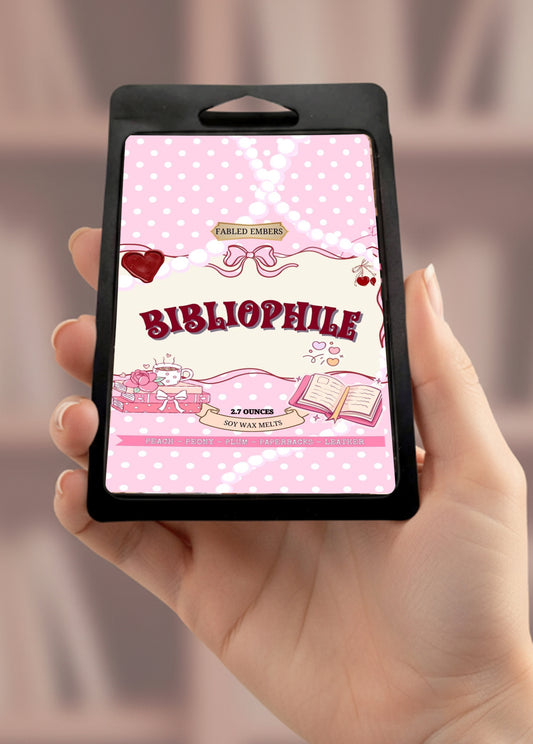 Hand holding a wax melt labeled 'Bibliophile' with a pink and white design.