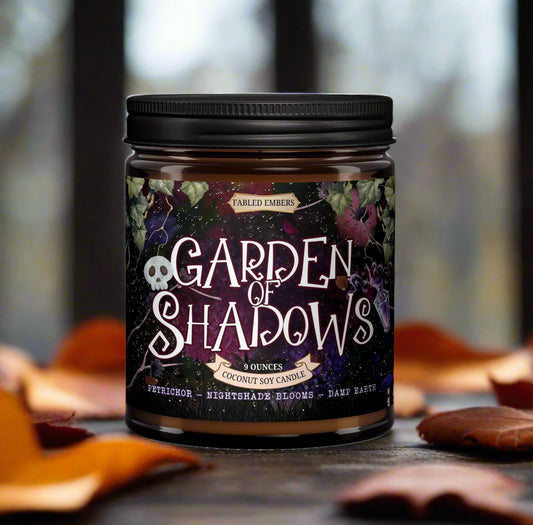 Candle jar labeled 'Garden of Shadows' with a dark label featuring text and graphics, set against a blurred natural background.